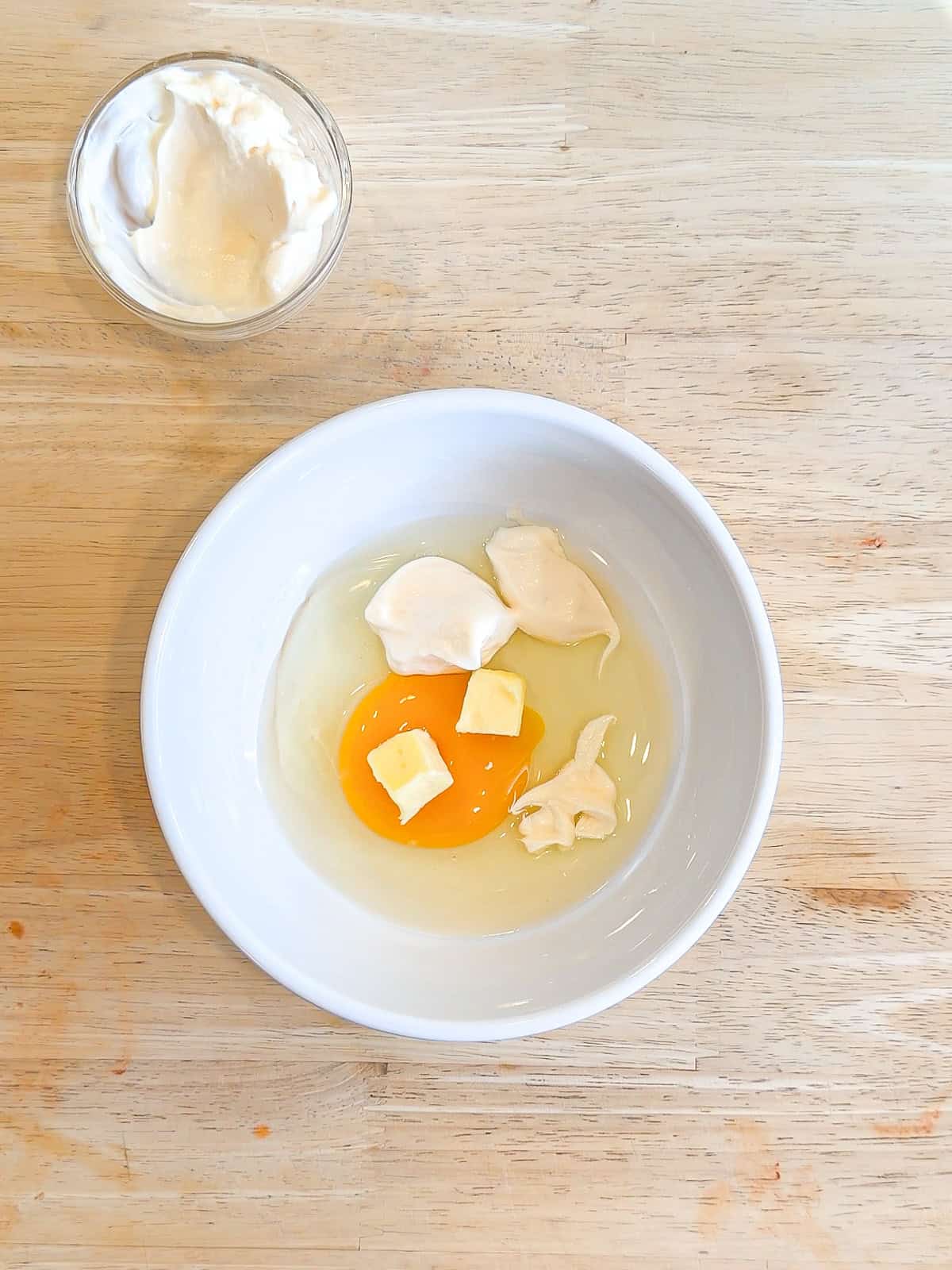Mayonnaise, softened butter, and an egg in a white bowl.