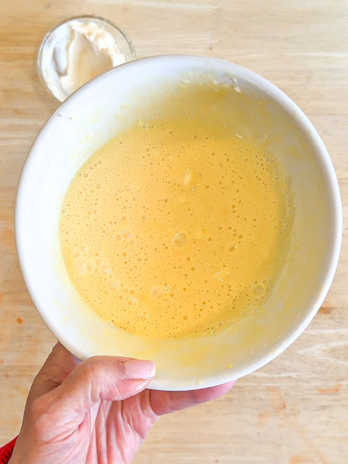 Whisking eggs, mayonnaise, and butter in a white bowl.